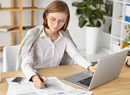 A lady wearing a white blouse filing for VAT registration in the UAE on her laptop.
